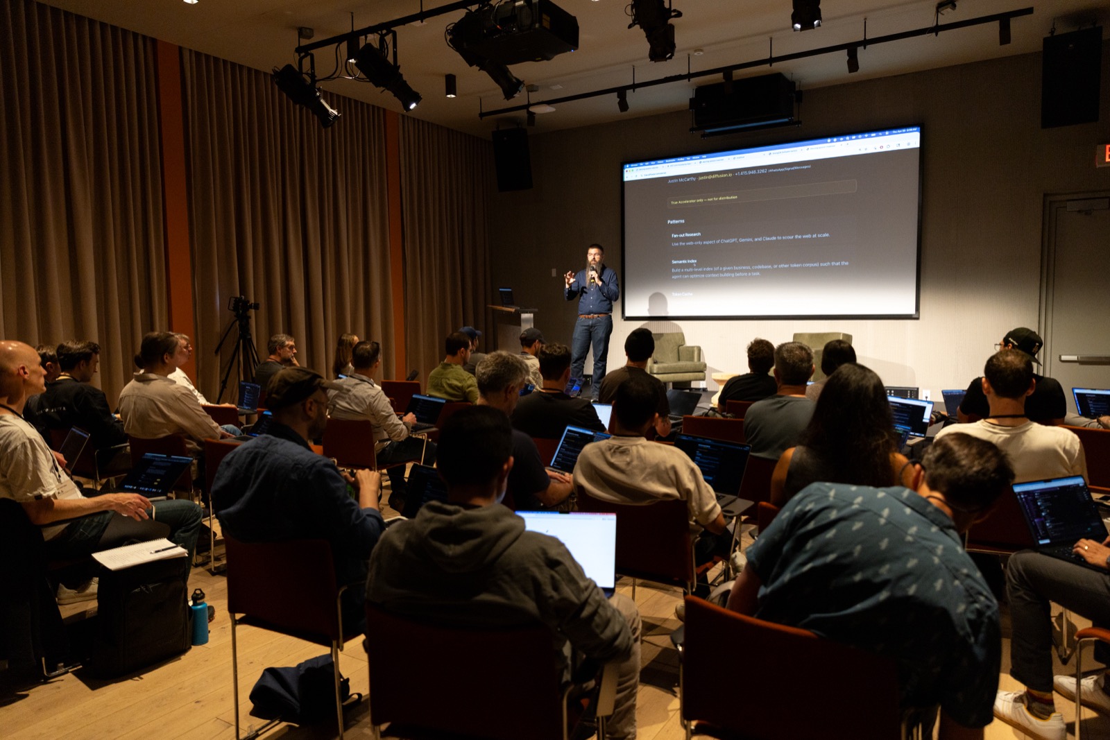 V1 AI Workflow Summit — speaker presenting live to a room of builders with laptops open